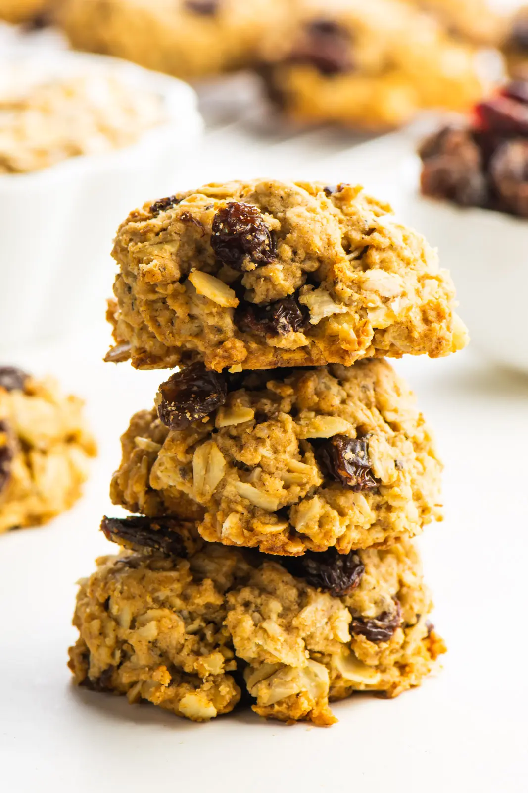 Three oatmeal cookies stacked with more cookies and ingredients around it.