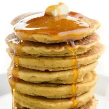 A stack of vegan pancakes with a pat of butter on top with maple syrup.