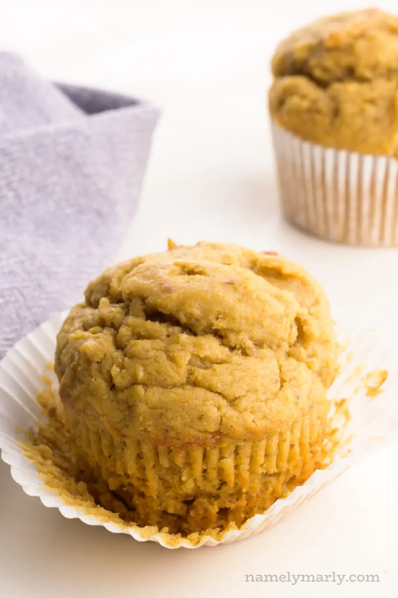A muffin has a napkin behind it with another muffin behind it too.