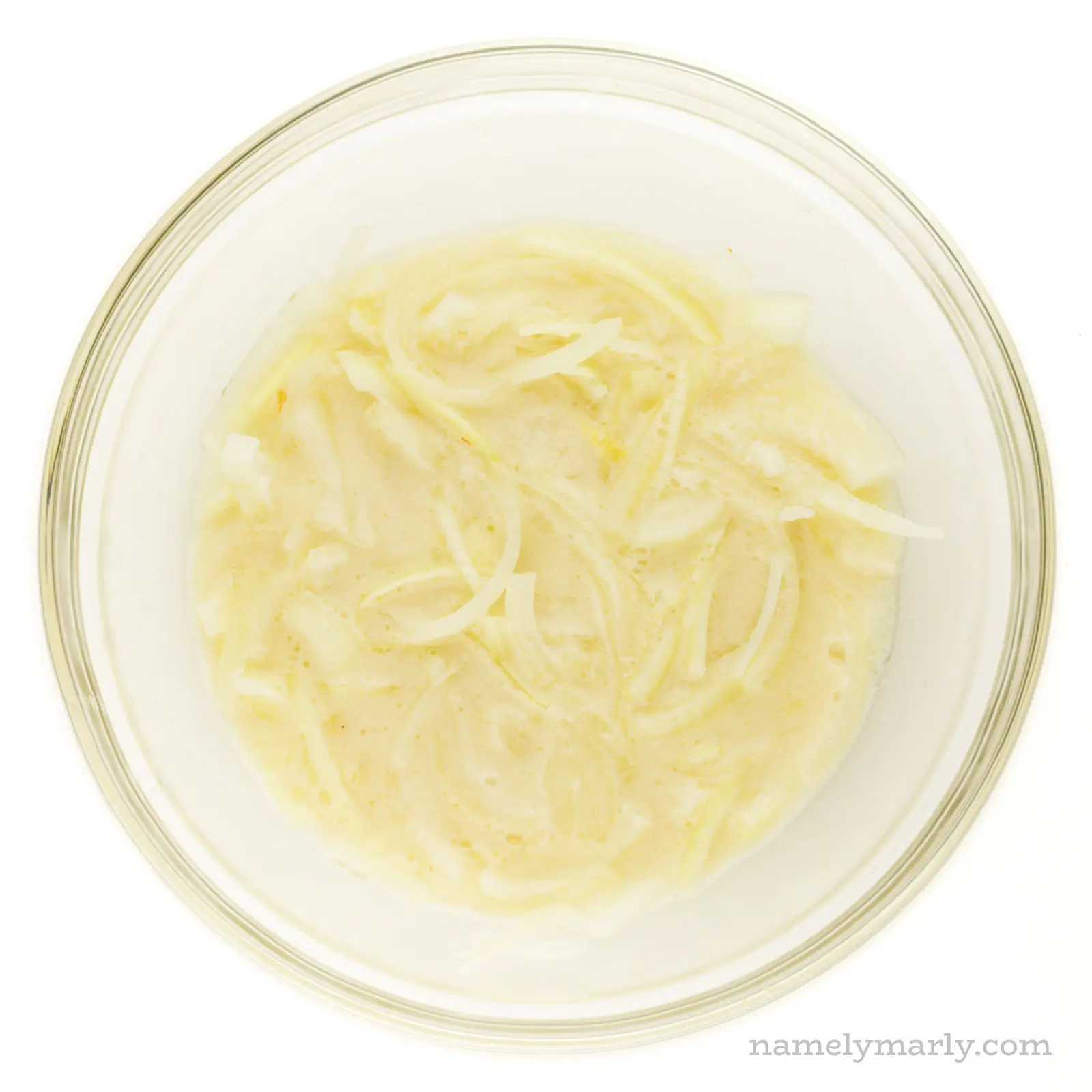 A bowl holds sliced onions are marinating in vegan buttermilk.