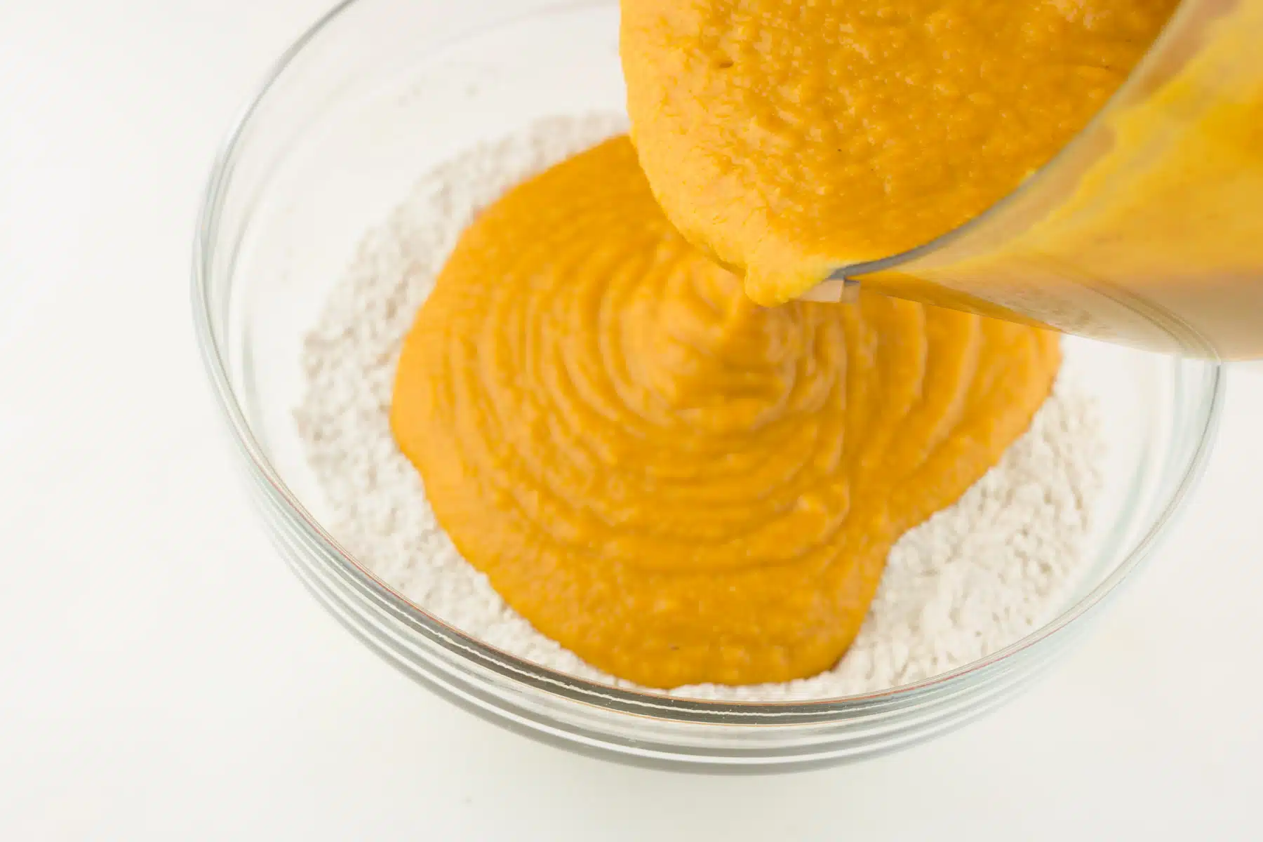 Pouring pumpkin batter into a bowl with flour.