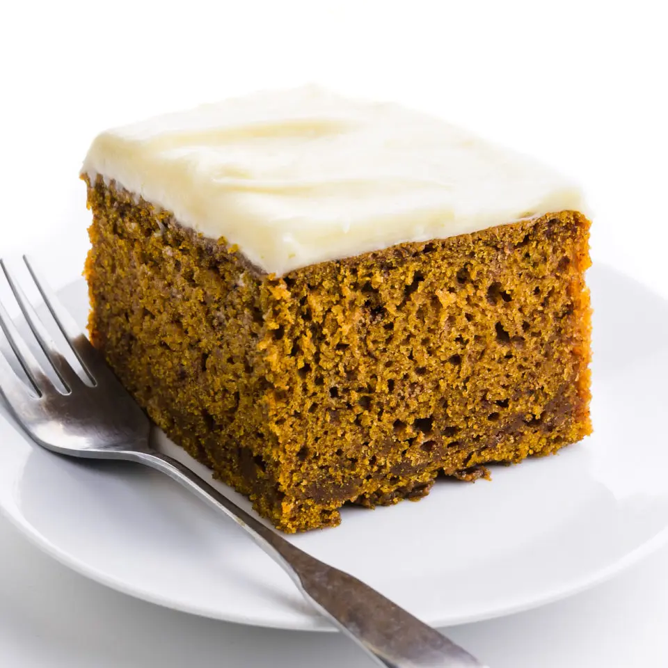 A single slice of vegan pumpkin cake on a plate with a fork beside it.