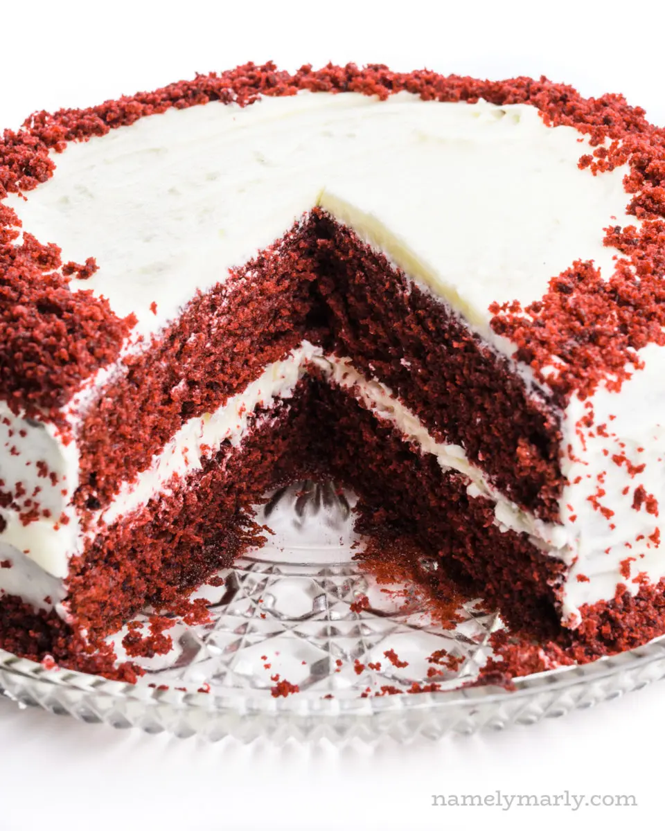 A layered vegan red velvet cake has several slices taken out of it.