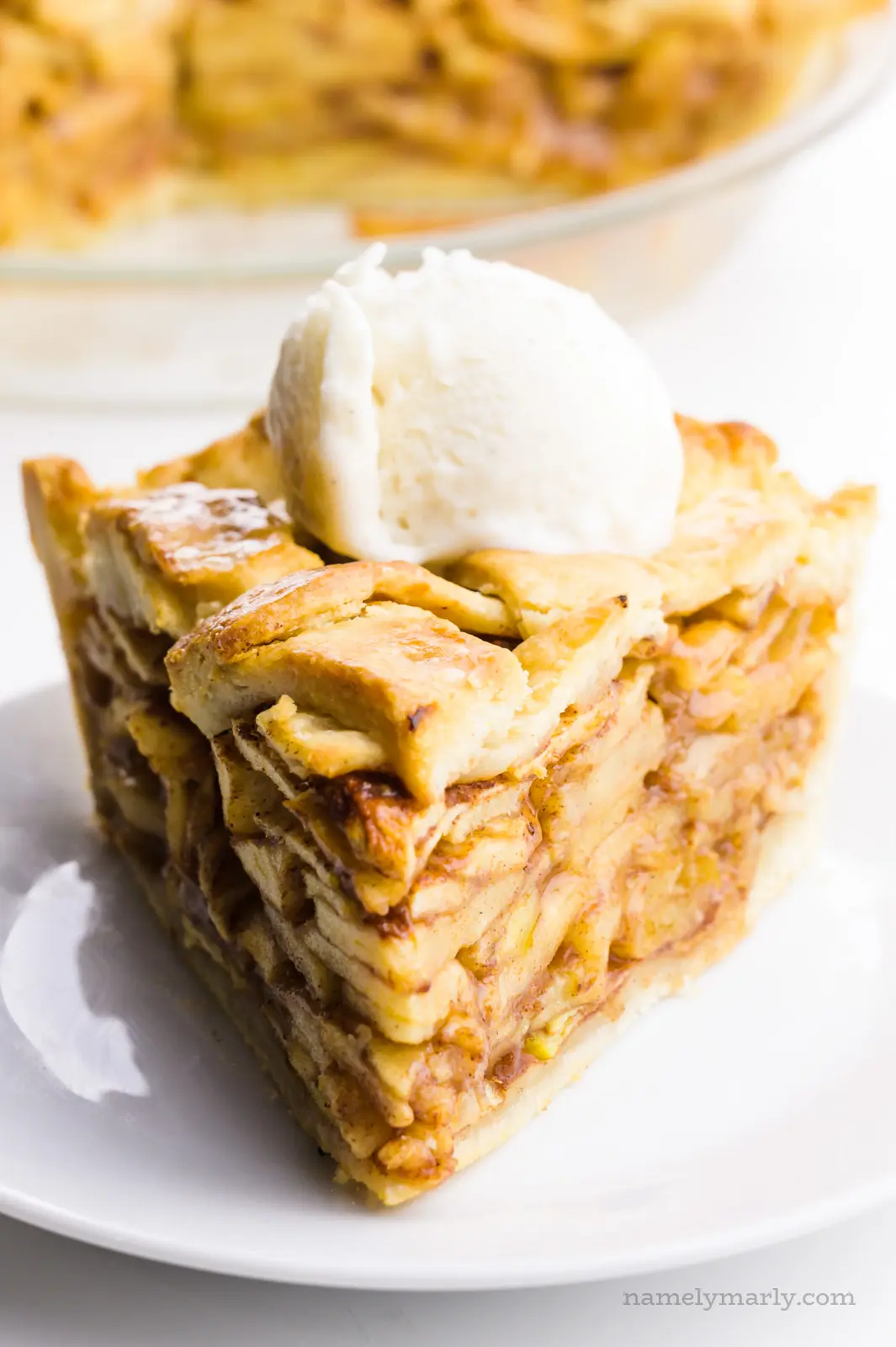 A slice of vegan apple pie has a scoop of ice cream on top and the rest of the pie behind it.