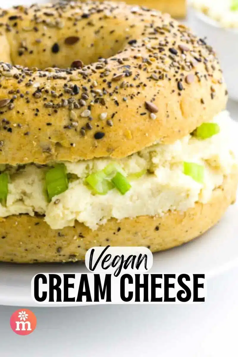 A bagel has cream cheese and green onions on it. The text reads, Vegan Cream Cheese.