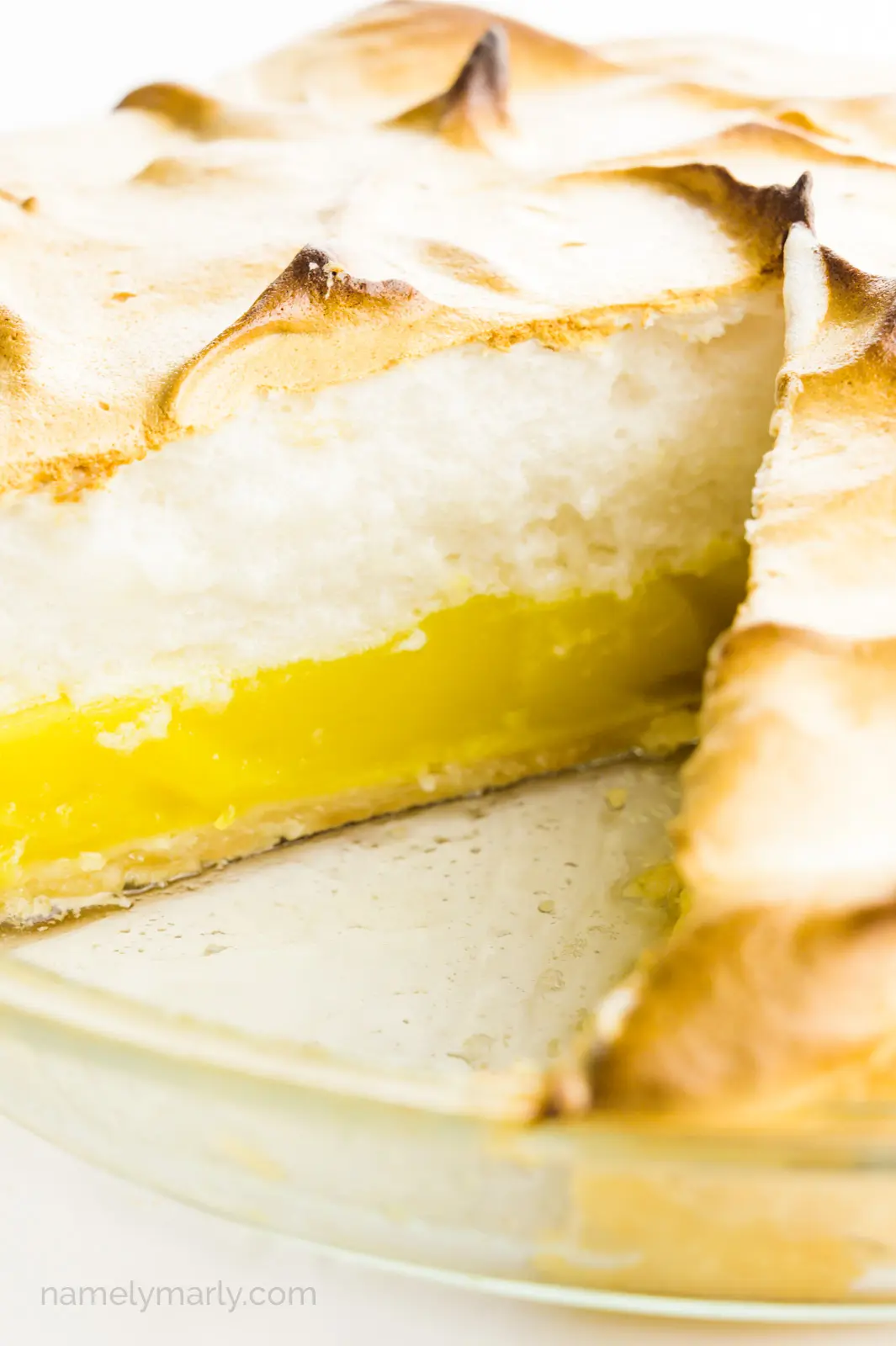 A lemon meringue pie has a slice cut out, showcasing layers of lemon curd and meringue on top.