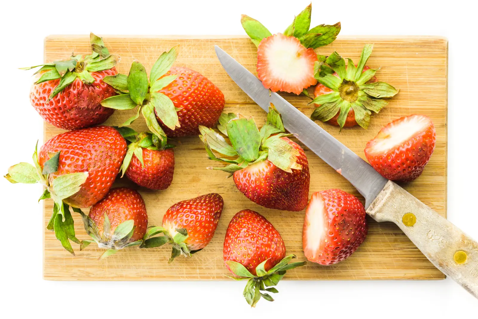 A cutting board has several sliced strawberries, sitting next to a knife.
