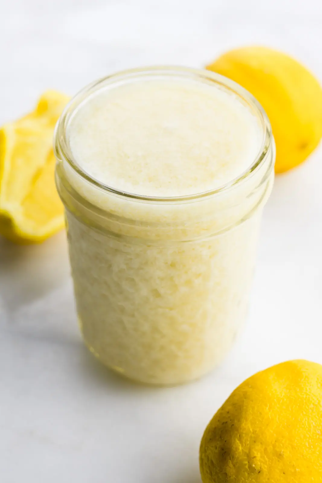 A small mason jar holds vegan buttermilk sitting around some lemons.