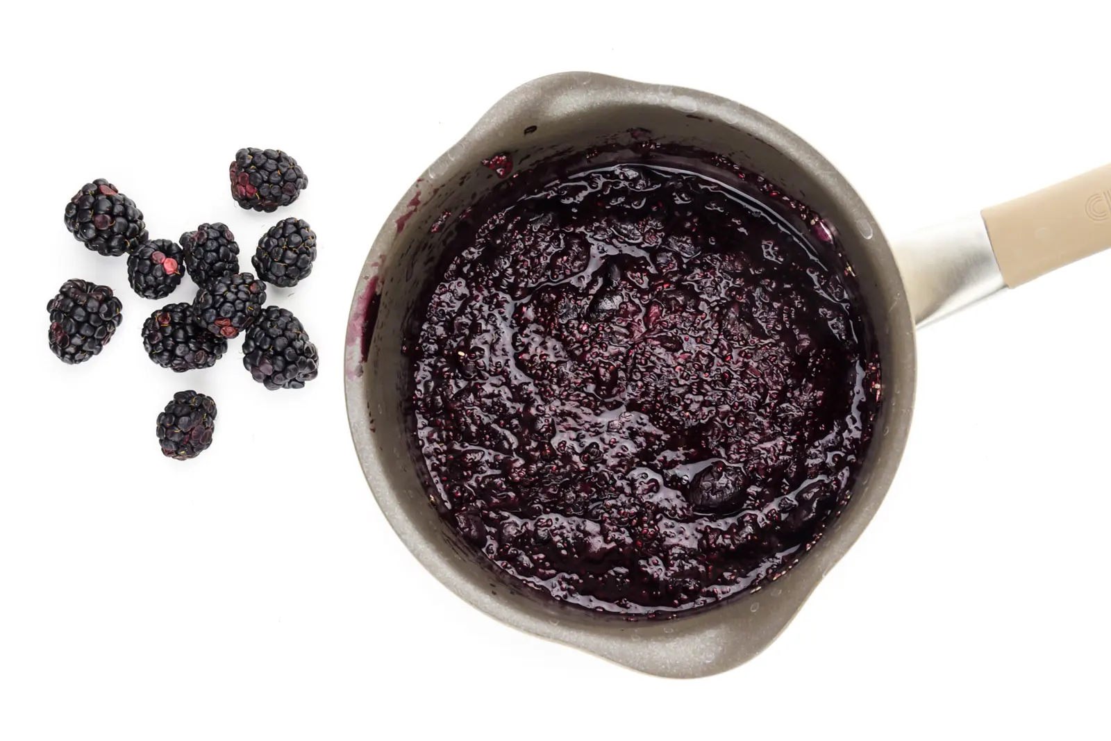 Looking down on a saucepan full of cooked blackberries. There re fresh blackberries beside the pan.