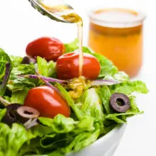 A spoon pours dressing over a salad. A jar with more dressing sits behind it.