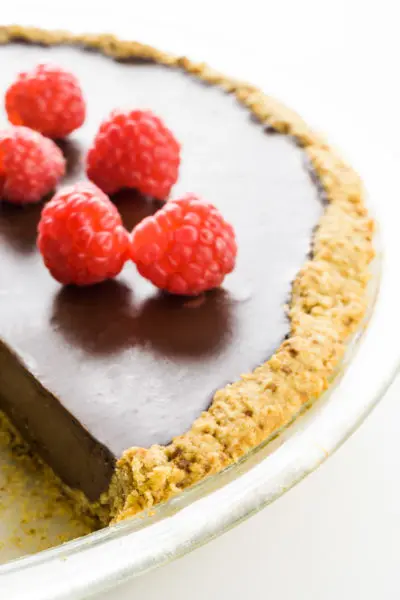 A chocolate pie with an oatmeal pie crust has several raspberries on top.