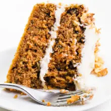 A slice of carrot cake sits on its side on a plate with a fork in front of it.