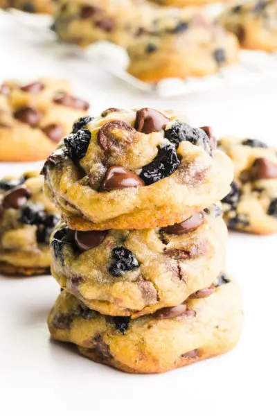 A stack of blueberry chocolate chip cookies sits in front of more cookies in the background.