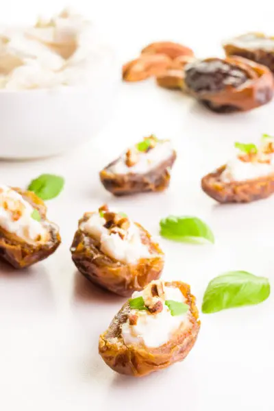 Several stuffed dates with basil leaves between them and cream cheese in a bowl behind it.