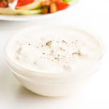 A bowl of vegan blue cheese dressing sits in front of a salad.