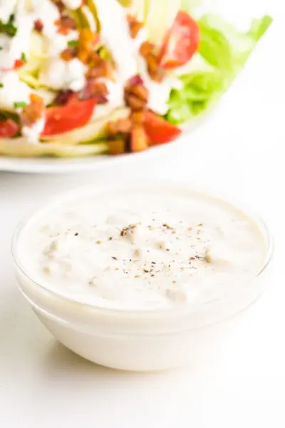 A bowl of vegan blue cheese dressing sits in front of a salad with dressing and toppings.