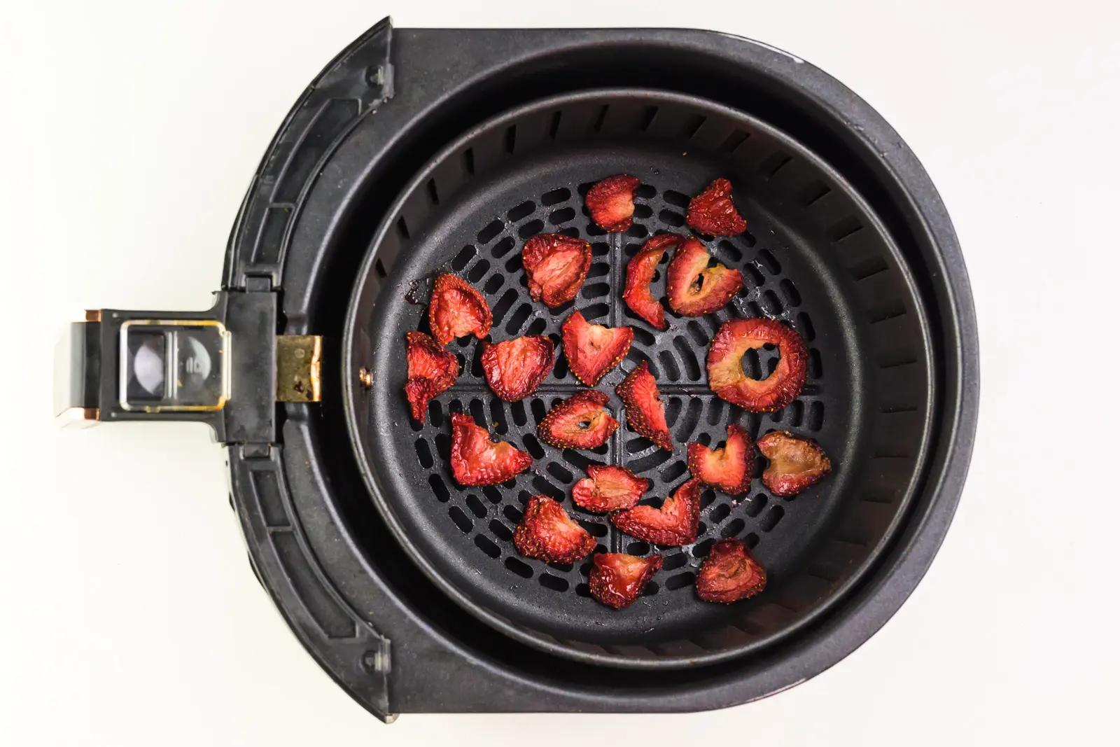 Dried strawberry slices are in the bottom of an air fryer basket.