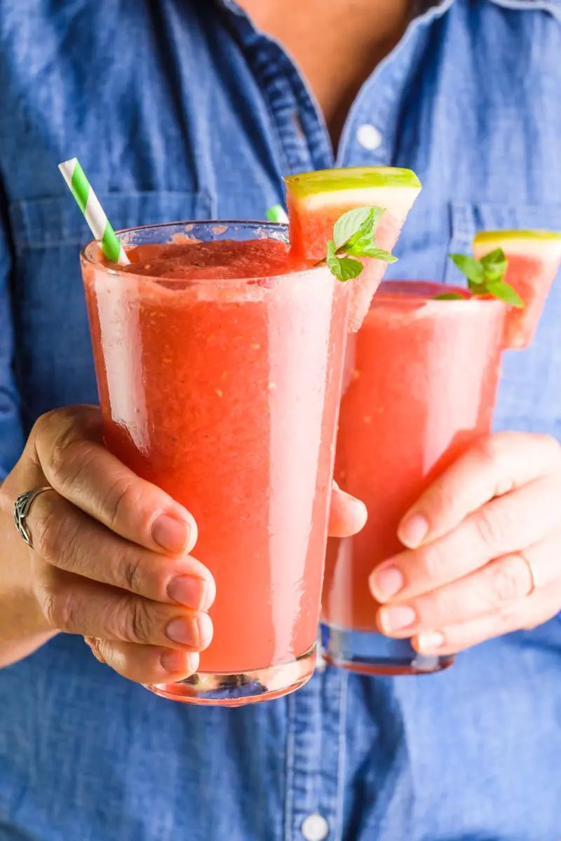 A woman in a jean shirt holds two glasses of watermelon slushie beverages.