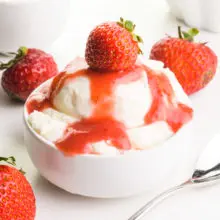 A bowl of ice cream is topped with a strawberry sauce and fresh strawberries.