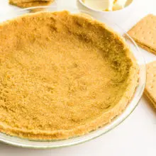 A graham cracker crust is in a glass pie pan. there are graham crackers and butter around it.