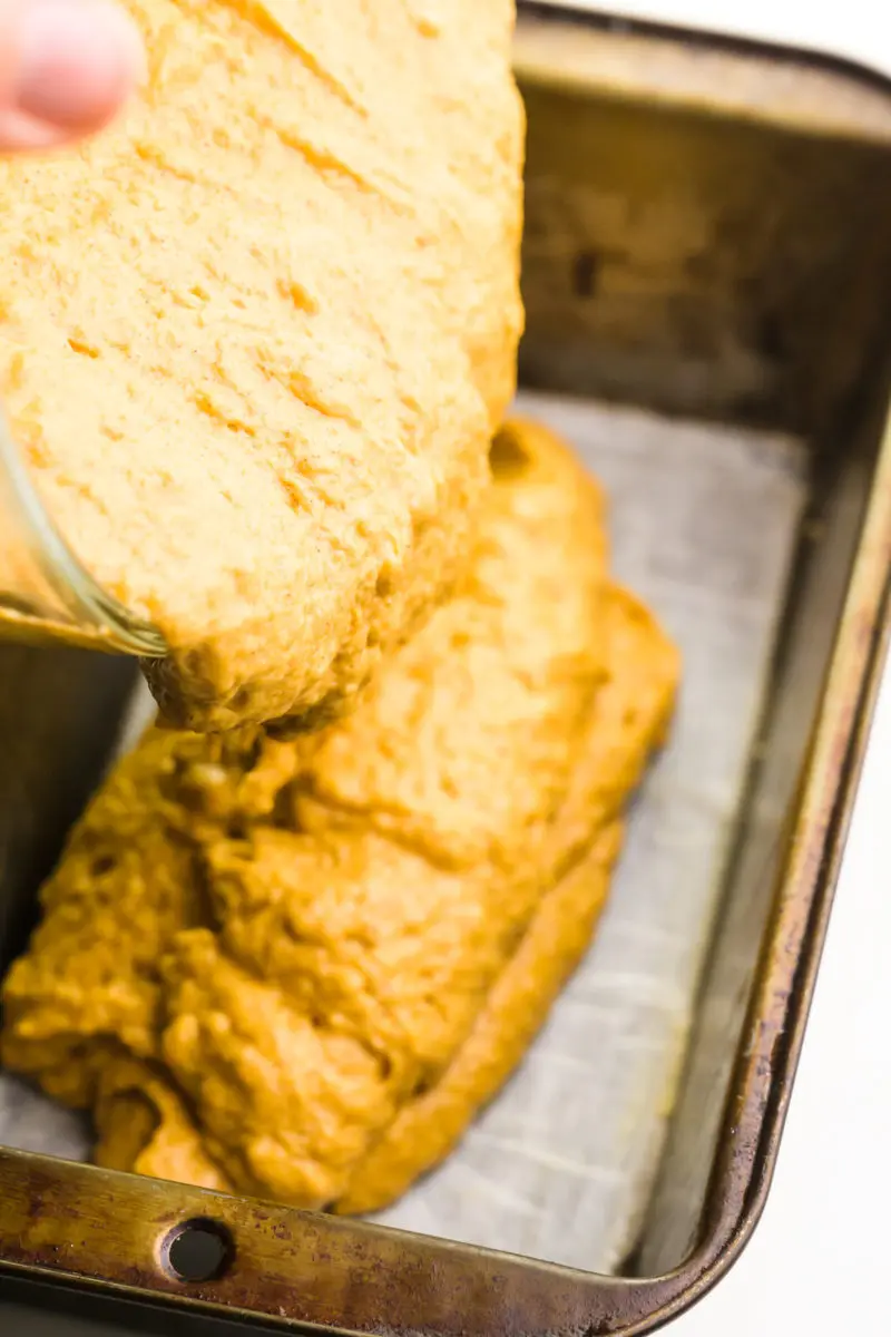 A batter is being poured into a loaf pan lined with parchment paper in the bottom.