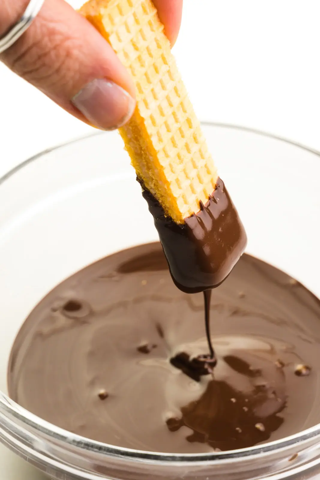 A hand holds a cookie, dipping it in melted chocolate.