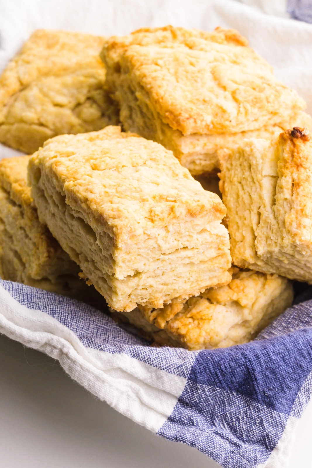 A blue kitchen towel is in a bowl holding several golden brown rectangle biscuits.