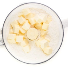 Vegan butter cubes have been added to a food processor bowl with a flour mixture.