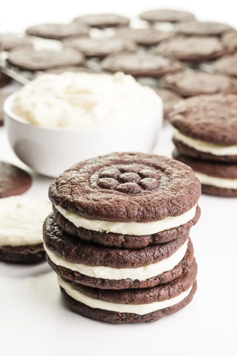 Homemade Oreo cookies are stacked in front of a bowl of filling and more cookies behind it.