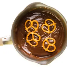 Looking down on a saucepan with melted chocolate. There are 4 pretzels on top of the melted chocolate.