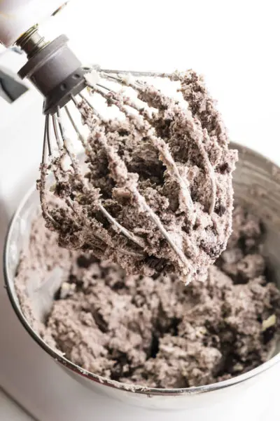 A stand mixer shows Oreo frosting in a whisk attachment and in the mixing bowl below it.