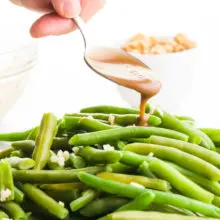 A hand holds a spoon drizzling balsamic glaze over steamed geen beans.