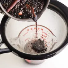 A pan is pouring syrup into a strainer into a smaller bowl.