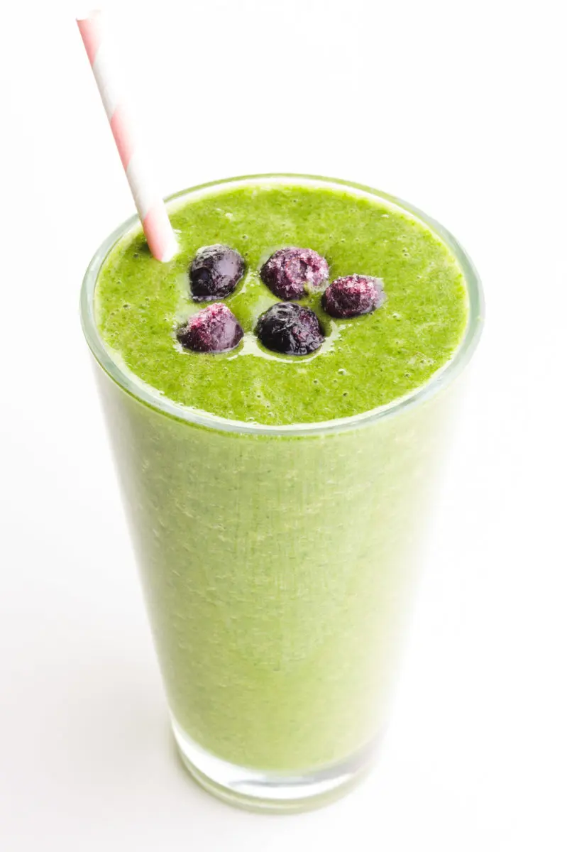 A green smoothie has blueberries on top and a pink straw on the side.