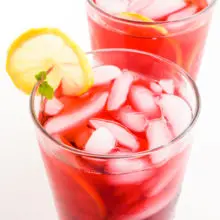 Two glasses of hibiscus tea have lemon slices on the side and ice in the glasses.