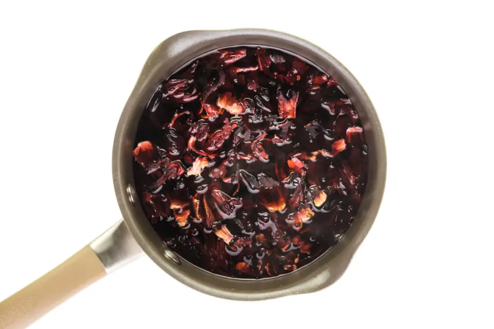 Ingredients are simmering in saucepan, including dried hibiscus flowers.