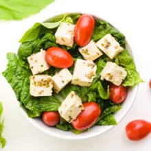 A bowl holds lettuce, cherry tomatoes, and cubes of tofu feta.
