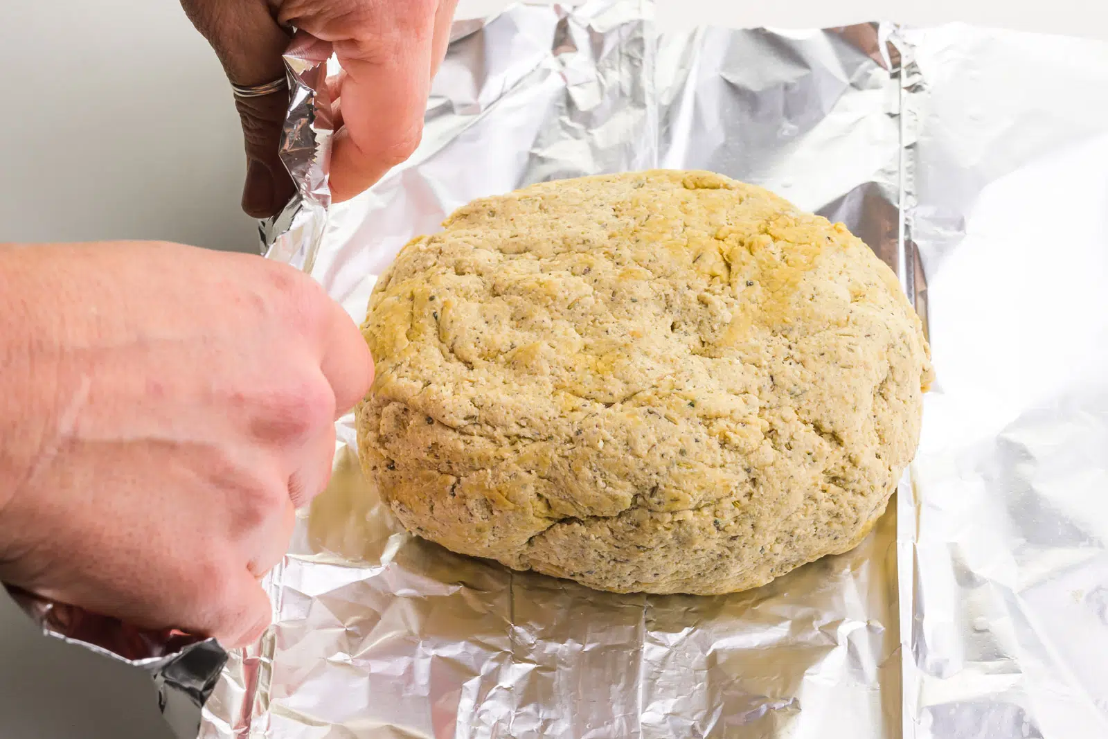 Hands are folding foil up around a vegan turkey loaf.