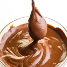 A spoon hovers over a bowl of vegan chocolate ganache. drizzling the chocolate sauce back into the bowl.