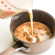 Milk is being poured into a saucepan with cocoa powder.