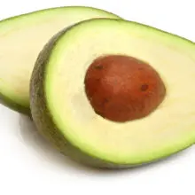 An avocado has been sliced in half, revealing the pit in side. The two halves are laying side-by-side.