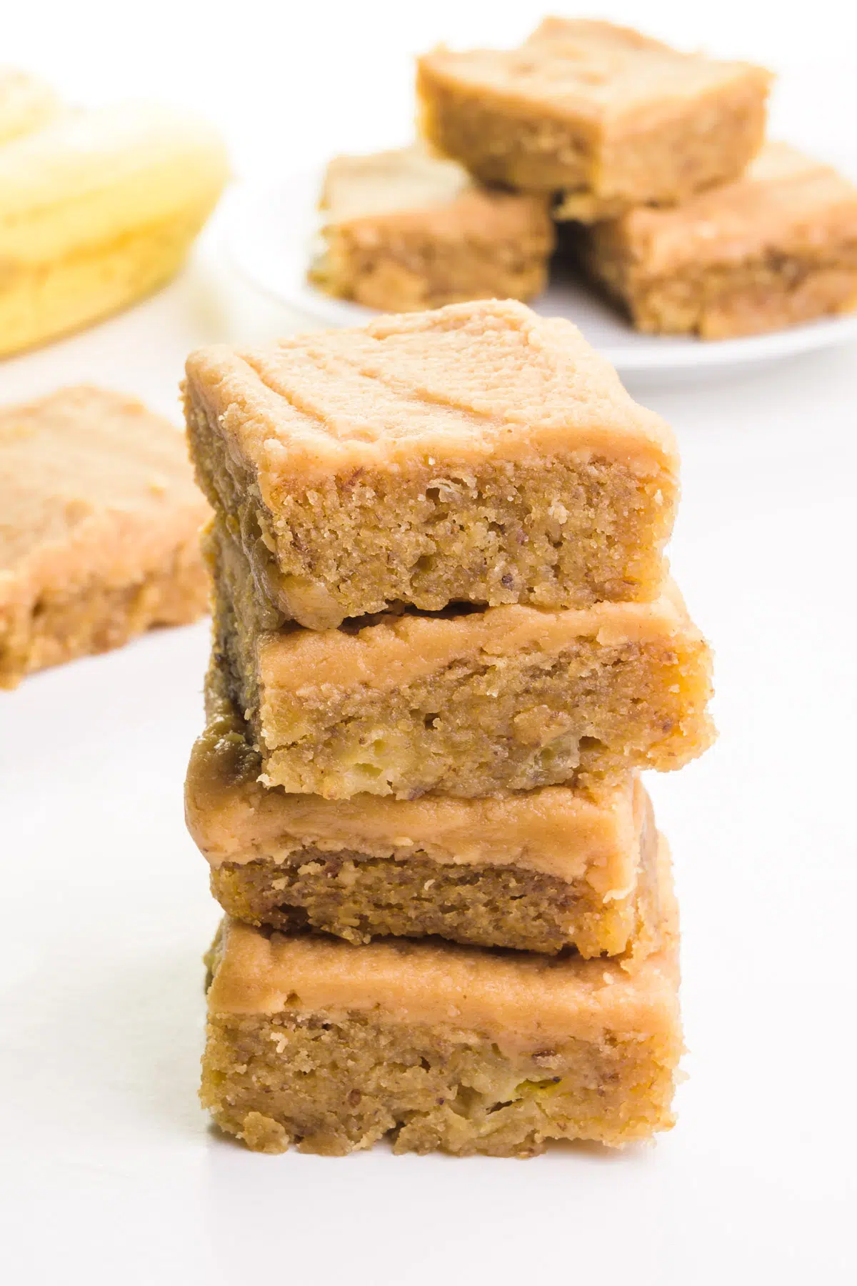 A stack of banana blondies with peanut butter frosting sits in front of more slices and bananas in the background.