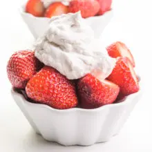 A bowl of strawberries is garnished with fluffy coconut whip topping. There's another bowl of strawberries in the background.