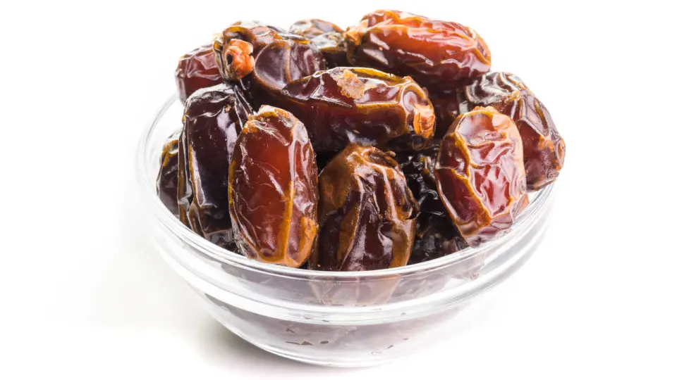 A mound of Medjool dates sit in a glass bowl on a white counter.