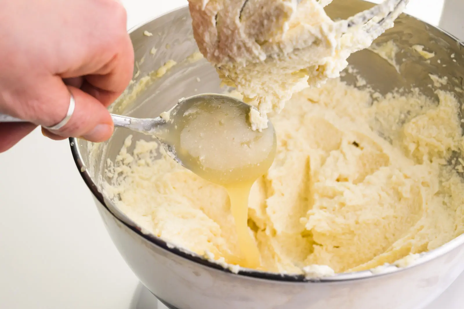 A hand holds a spoon, dripping a creamy mixture in with whipped butter.