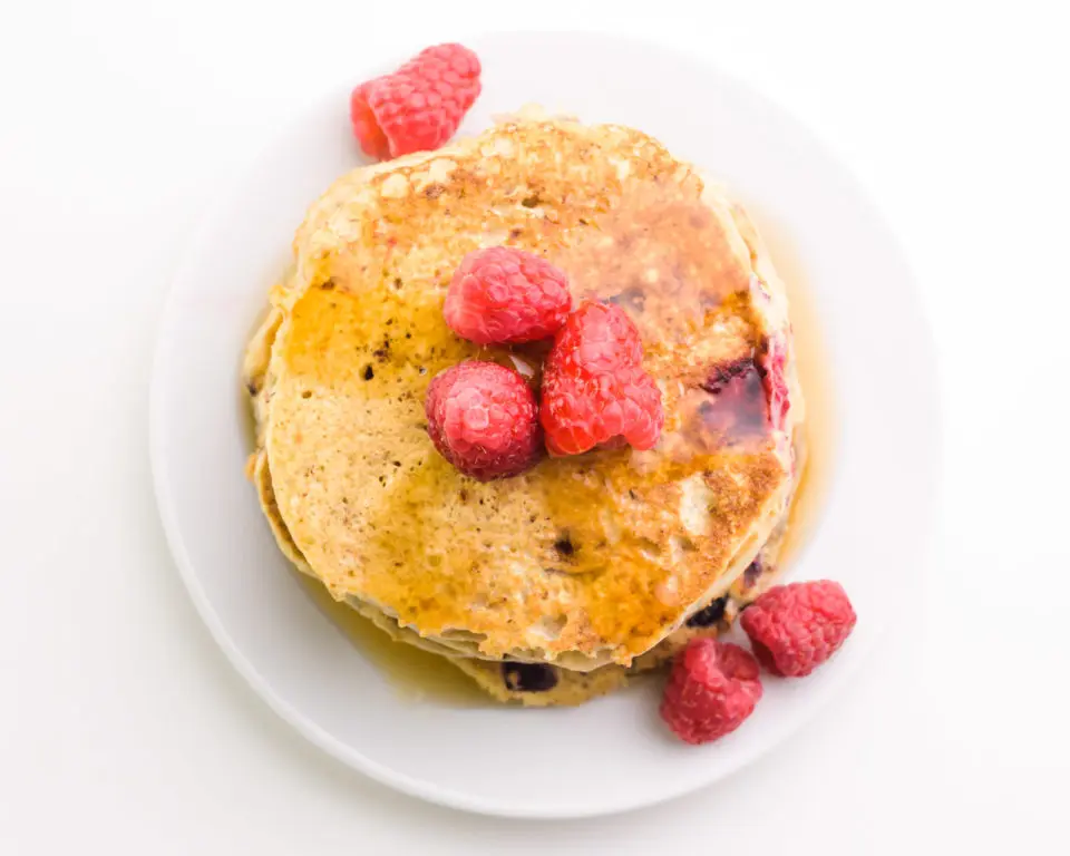 Looking down on a plate full of pancakes with raspberries on top and on the side.
