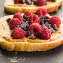 Slices of bread are on a griddle and topped with peanut butter, chocolate chips, and fresh raspberries.