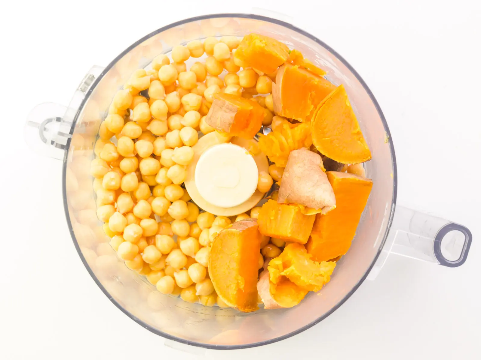 Chickpeas and chopped sweet potatoes are in the bottom of a food processor.