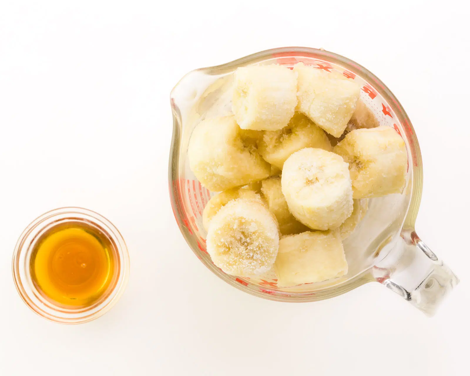 A pyrex measuring glass full of sliced bananas sits next to a small bowl of maple syrup.