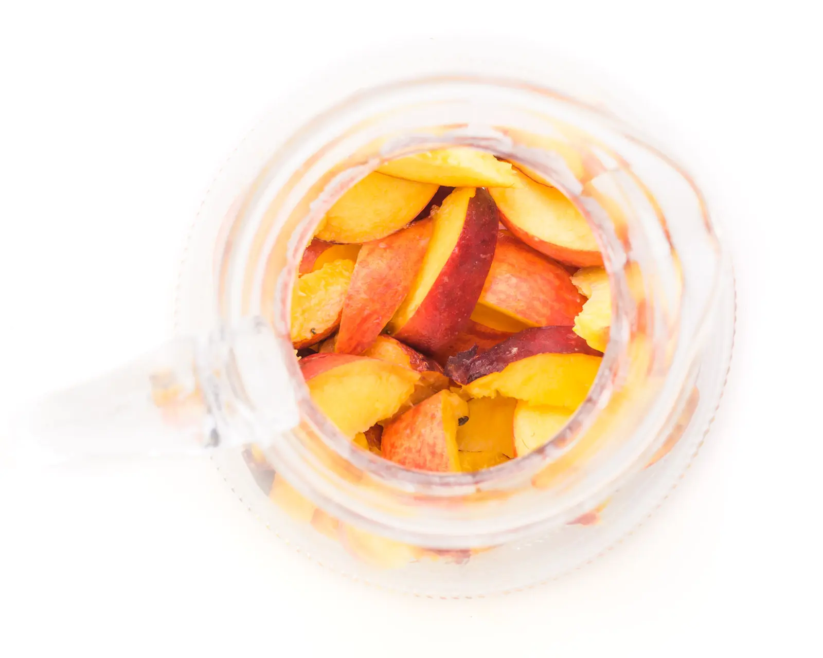 Looking gown on a pitcher full of sliced peaches.